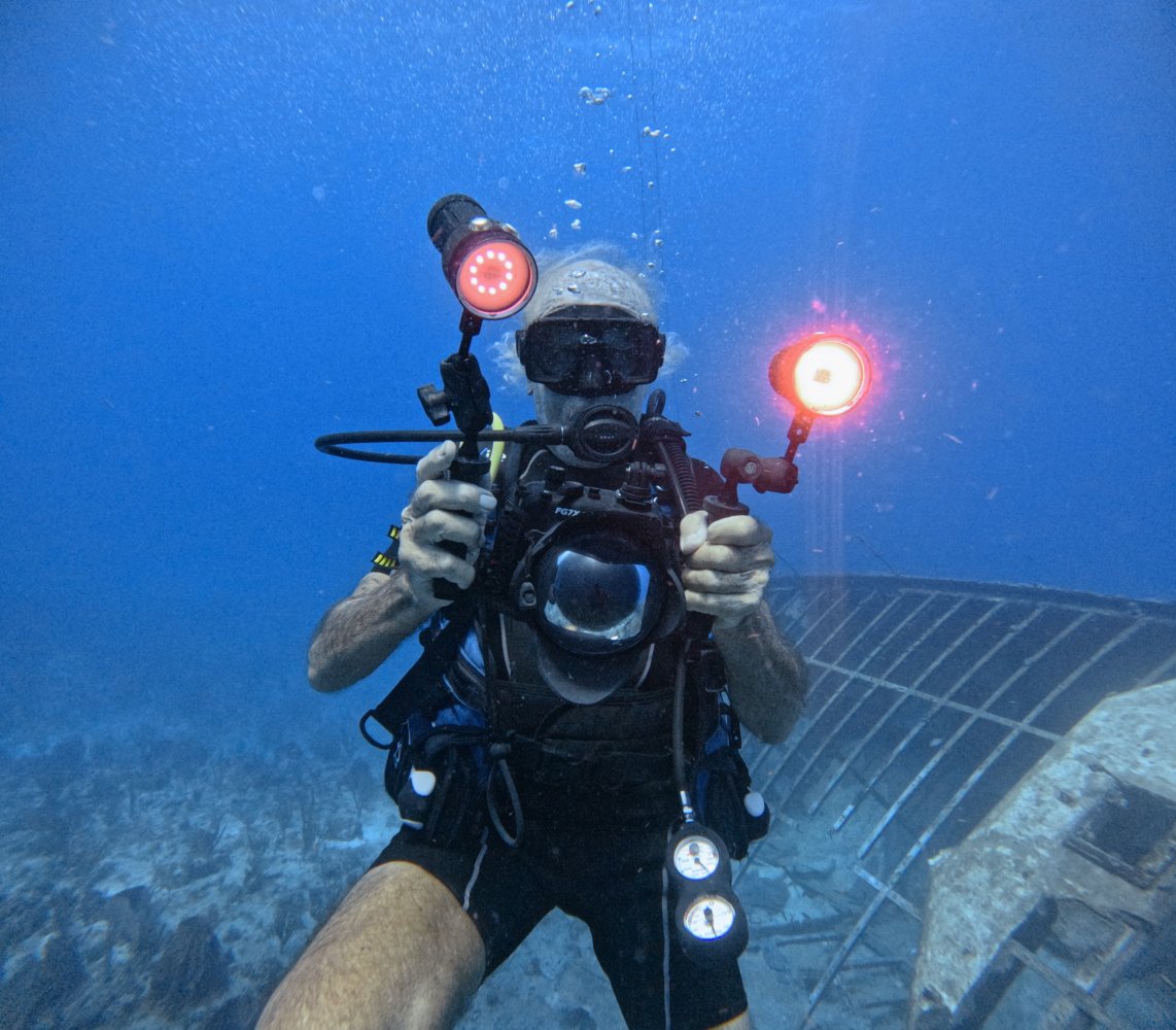 Underwater diver with camera and lights near wreck.
