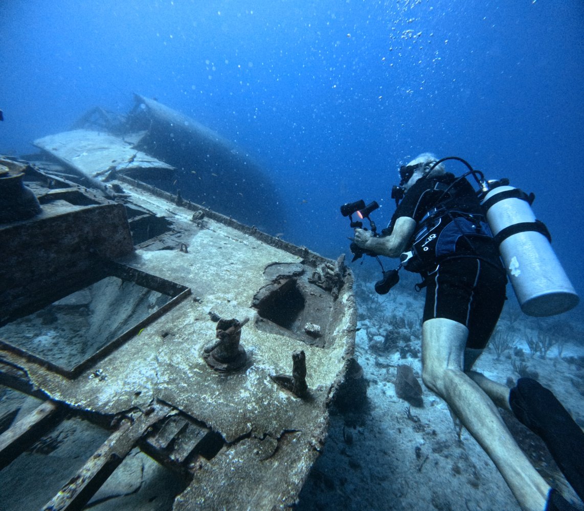 Scuba diver exploring a shipwreck underwater with a camera in hand.