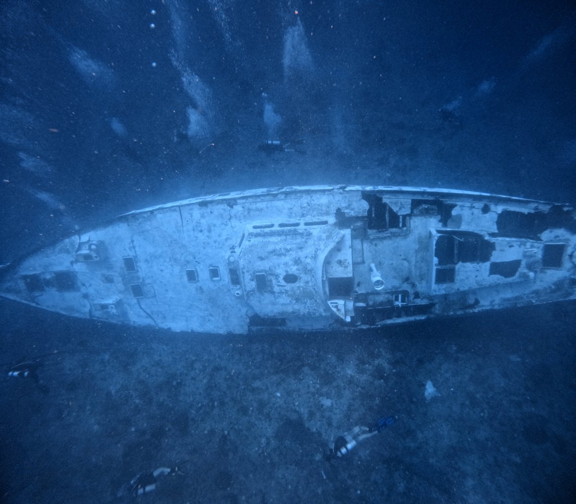 Underwater view of a sunken ship with divers exploring the wreckage.