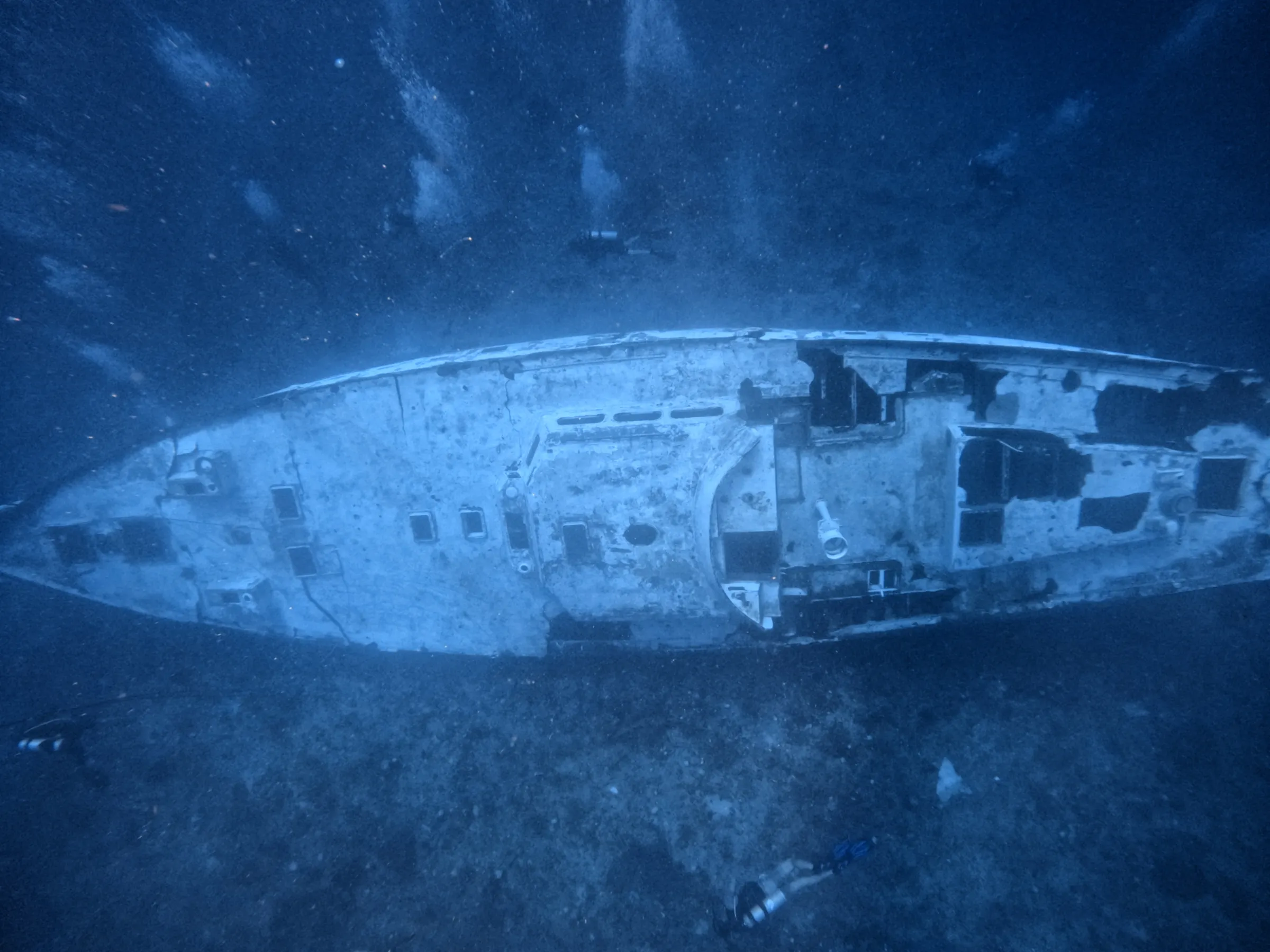 Underwater view of a sunken ship with divers exploring the wreckage.